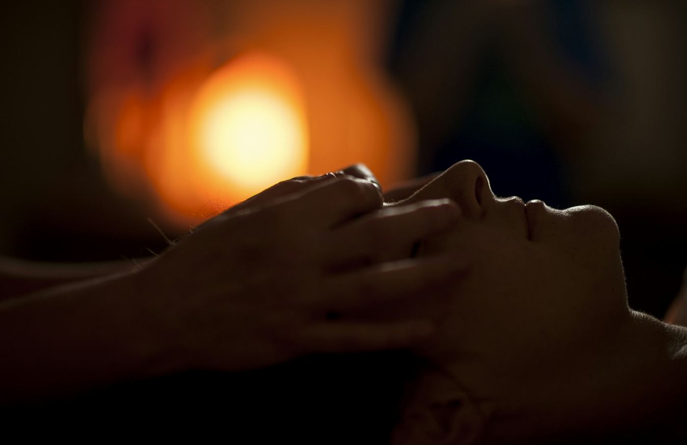 A masseur's hands on a client's temples in a warm half-light